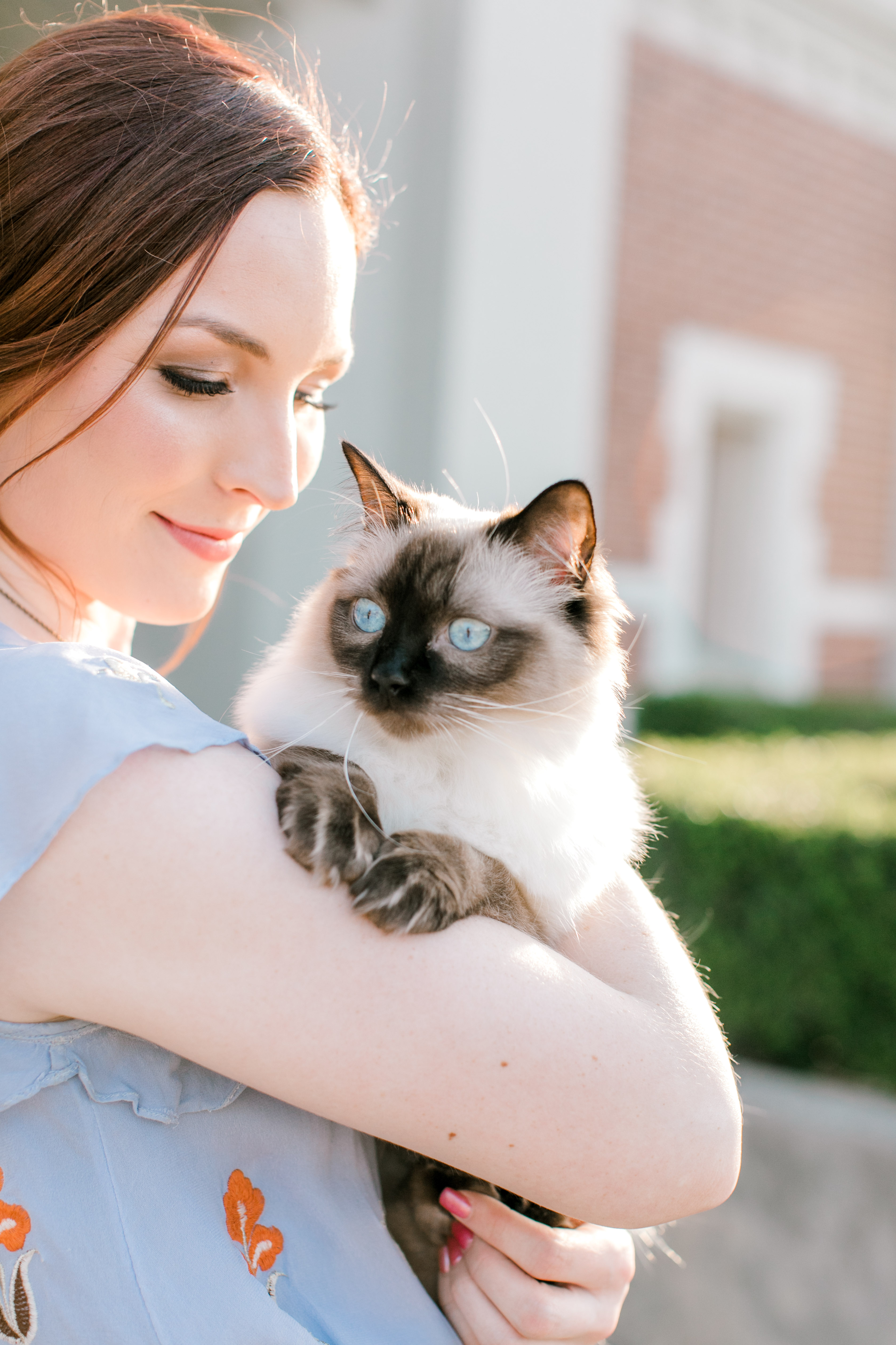 ou senior holds cat with blue eyes in front of jacobson hall visitors center