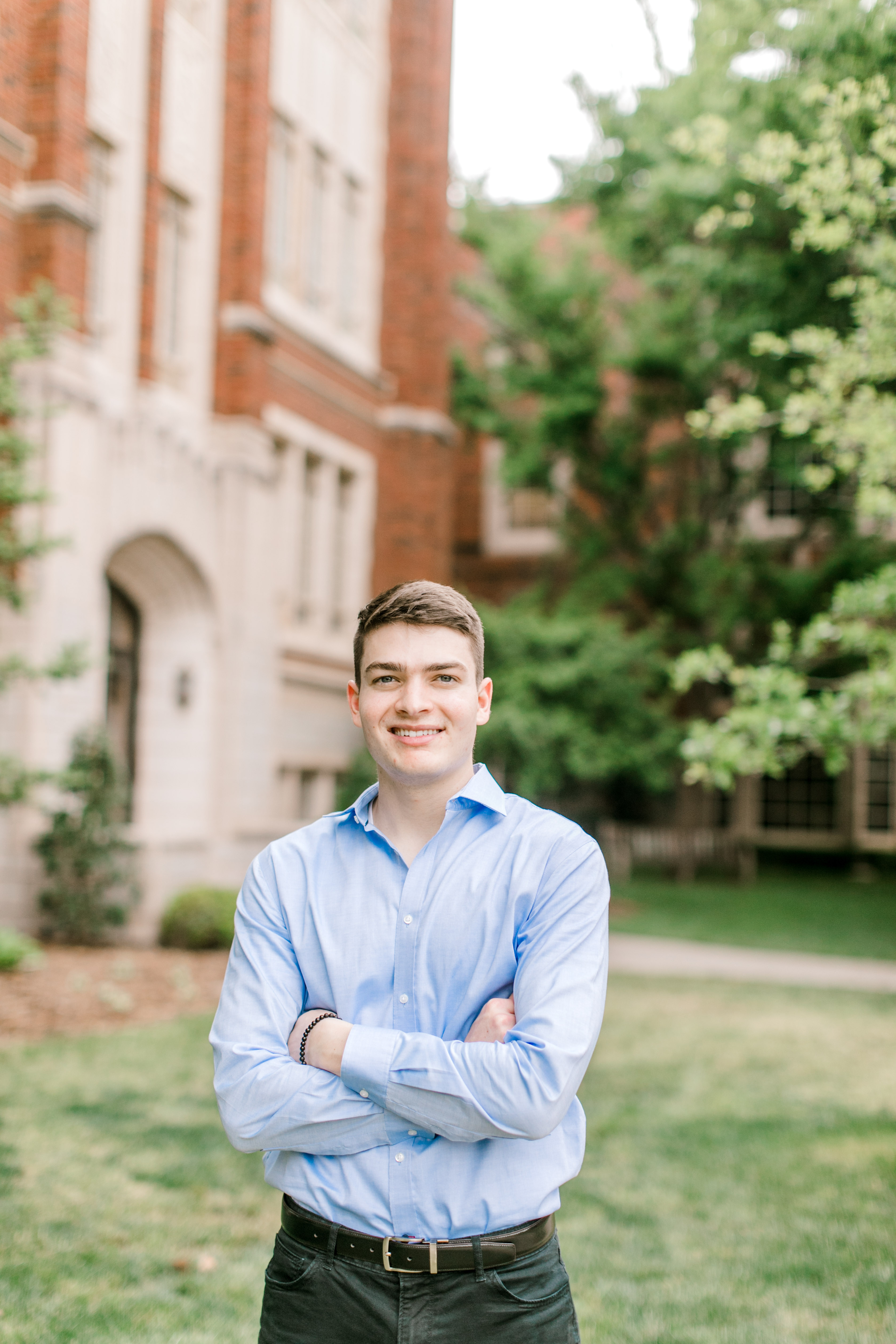 brunette college boy stands in front of greenery on ou campus for ou graduation photos
