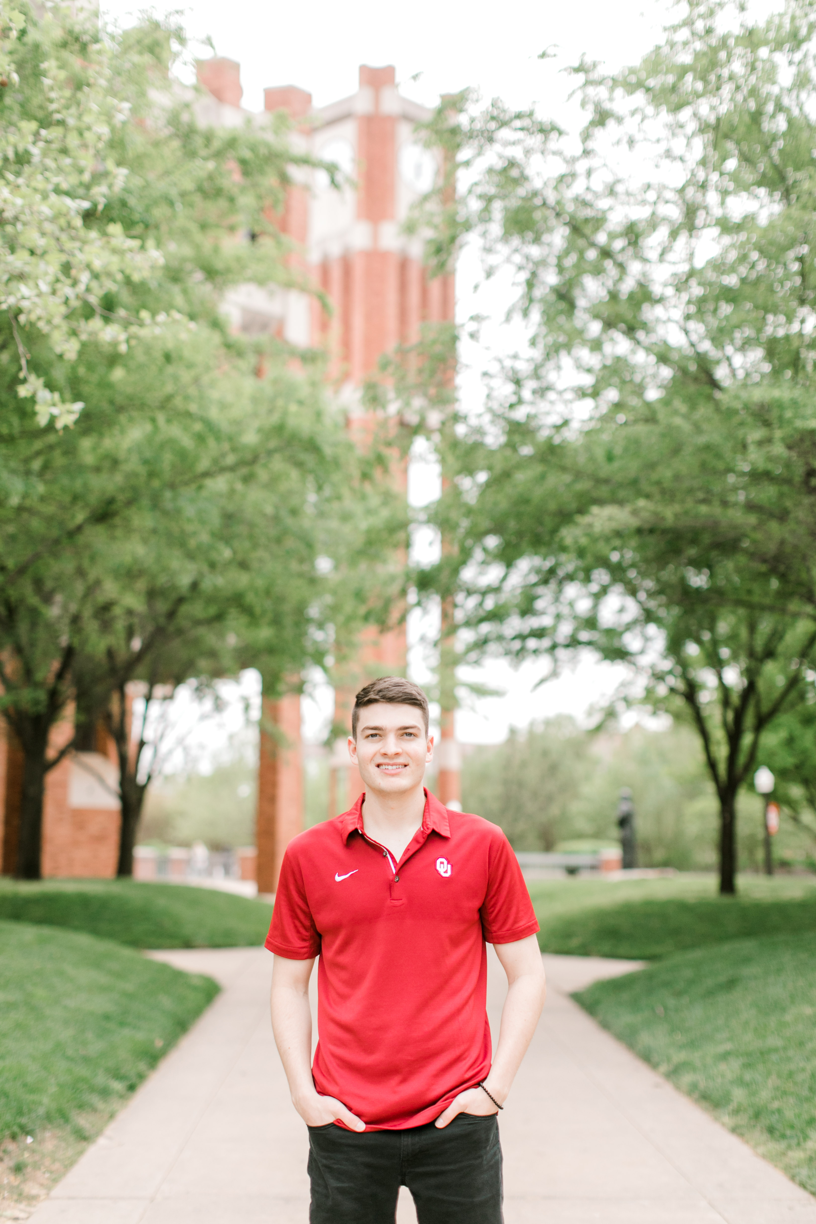 brunette college boy stands in front of greenery on ou campus for ou graduation photos