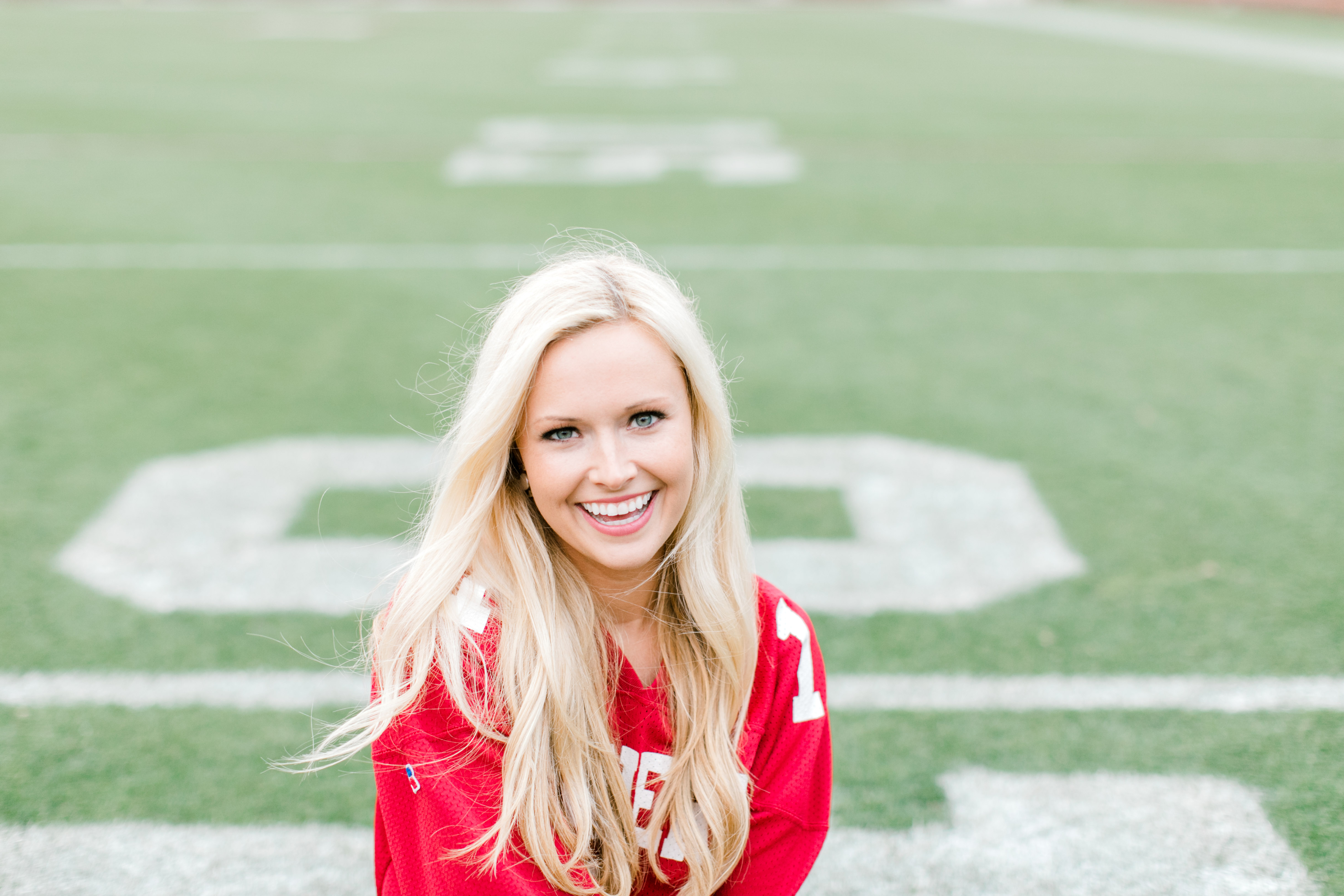 blonde college senior sits in jersey on football field in norman ok senior photographer