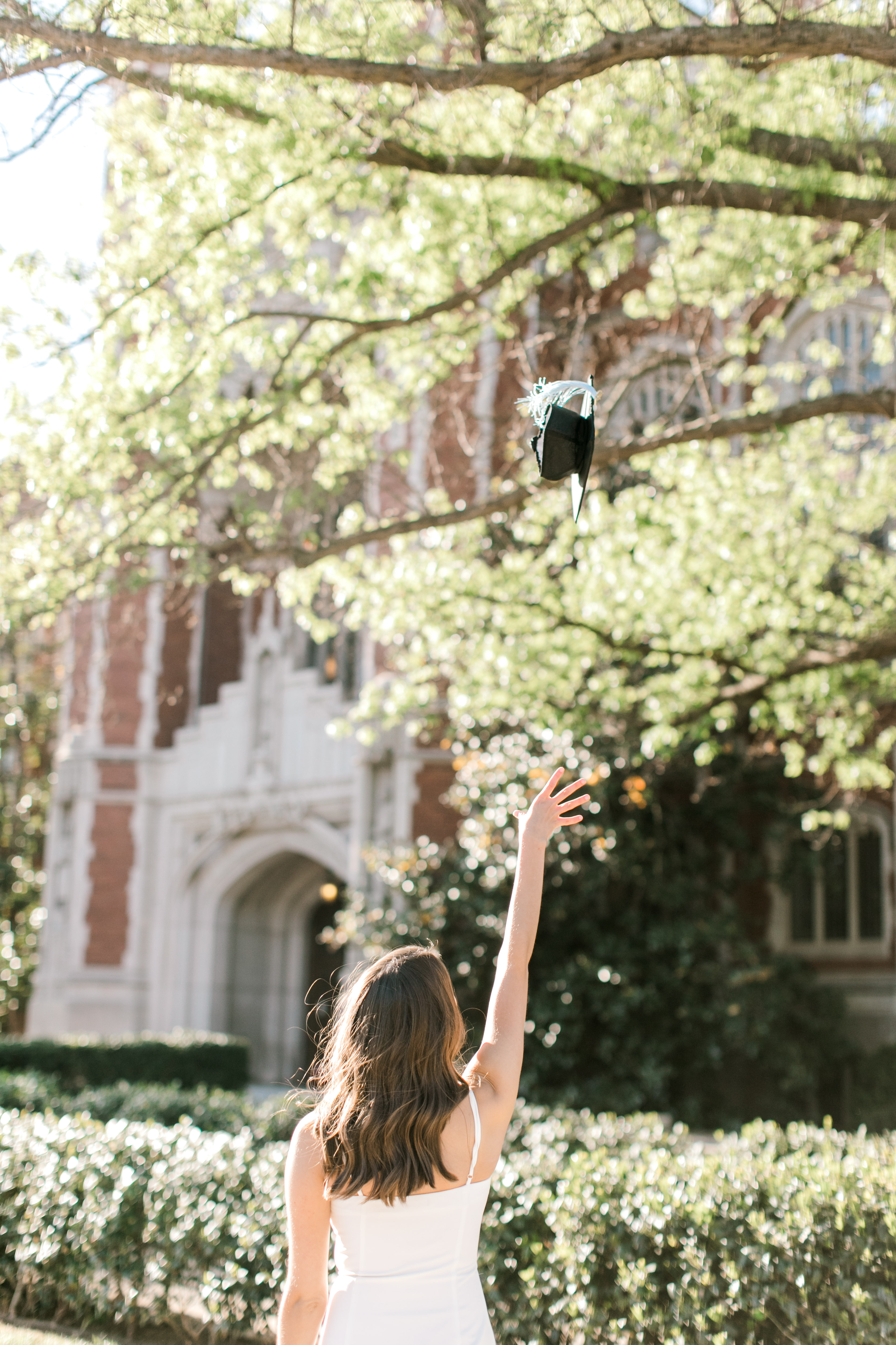 brunette senior throws graduation cap in front of library for senior photo ideas