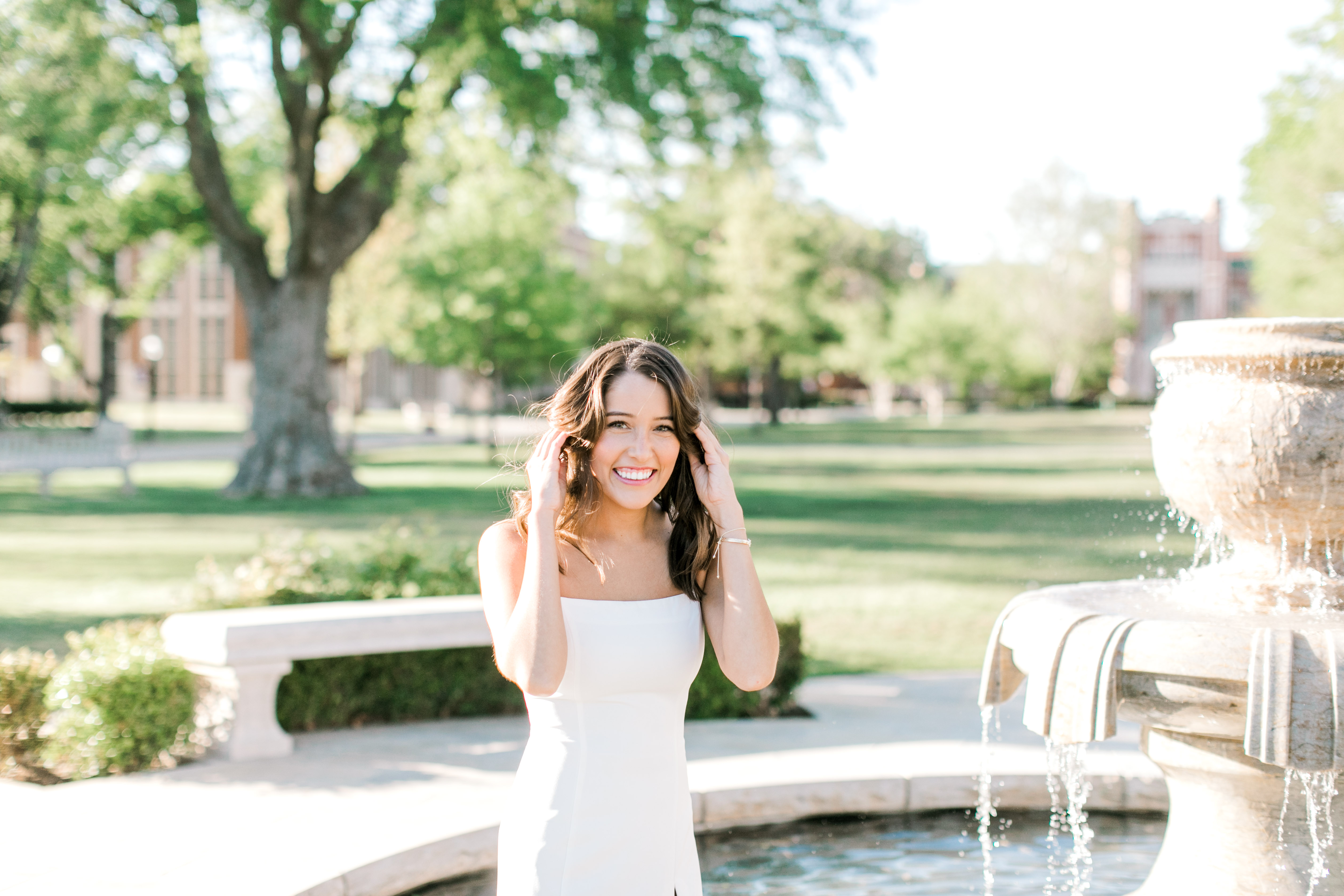 brunette ou senior laughs while standing in fountain for senior photo ideas