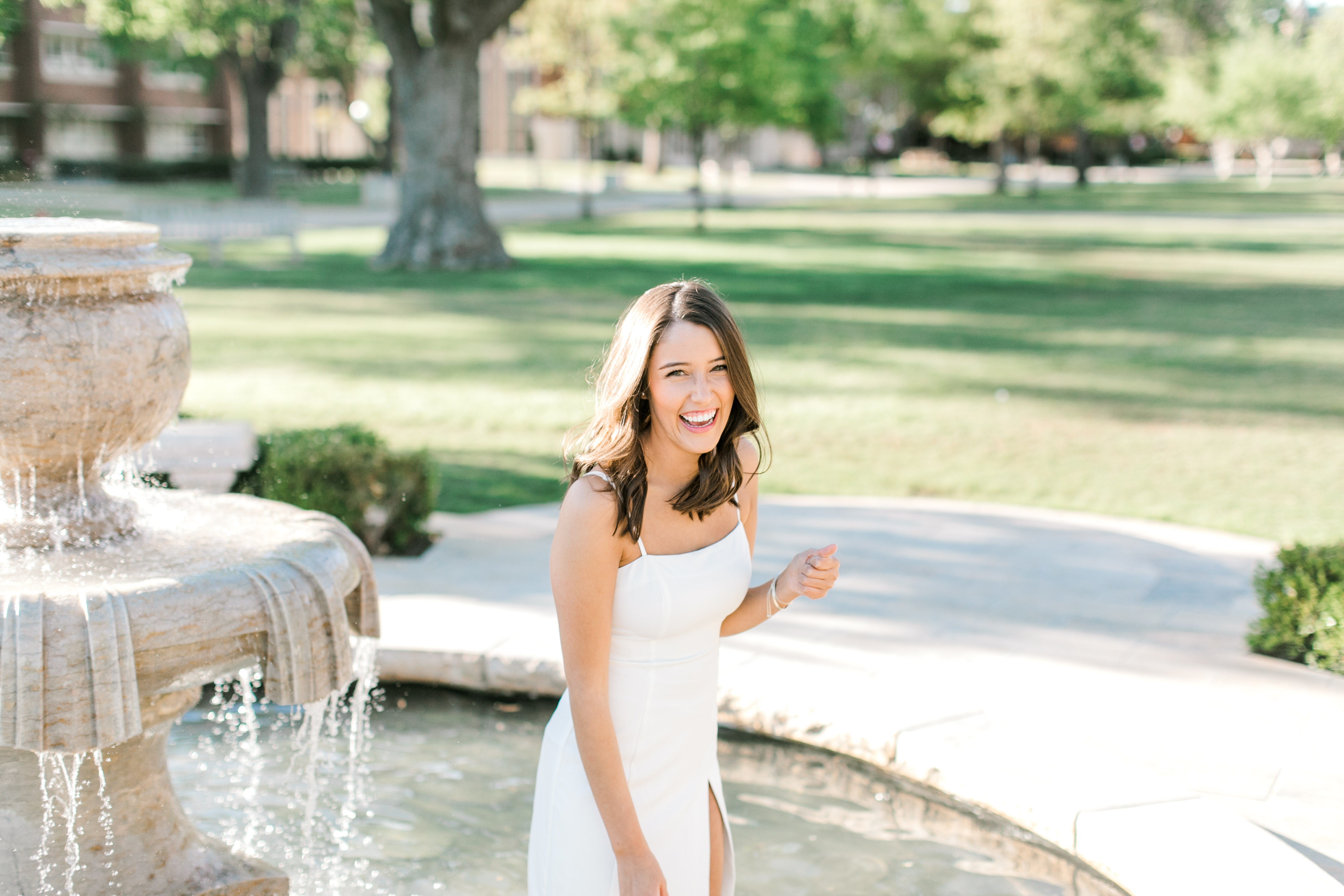 brunette ou senior laughs while standing in fountain for senior photo ideas