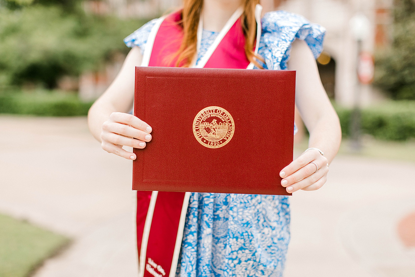 graduate holds diploma cover in front of bizzell memorial library for senior photos at OU