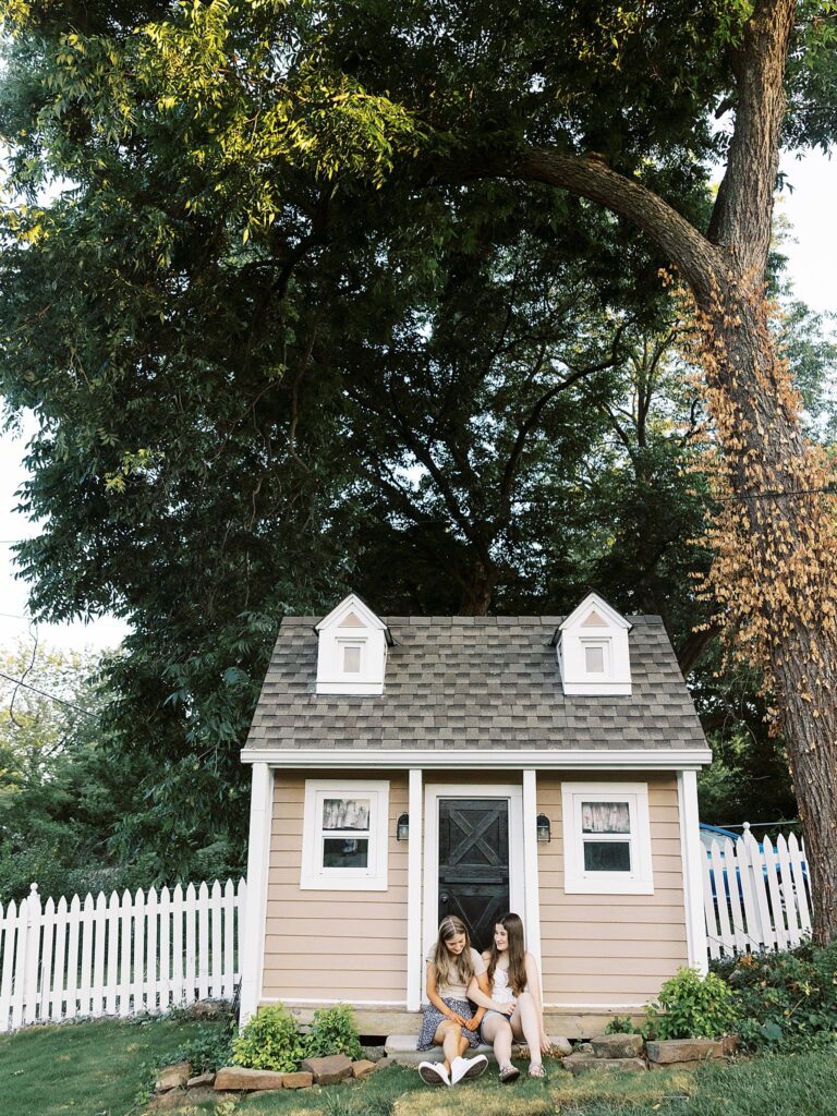 two teenage girls laughing in front of a custom built playhouse their dad made for them in their bartlesville home backyard