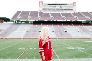 blonde college senior sits in jersey on football field in norman ok senior photographer