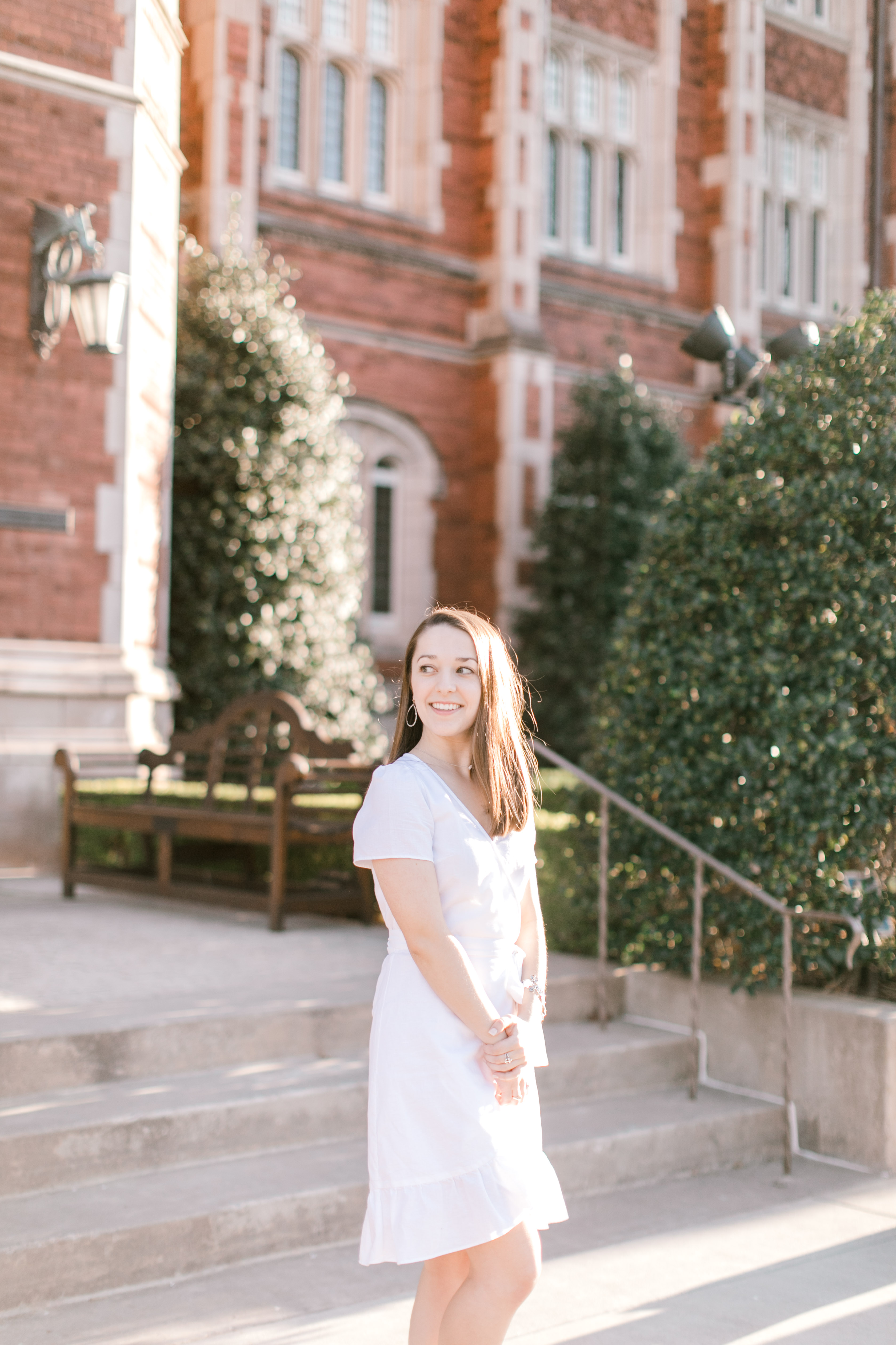 young senior stands in front of academic building on ou campus in white dress