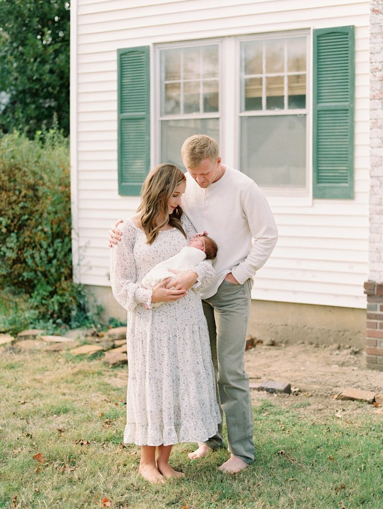 couple holds newborn baby in front of colonial home