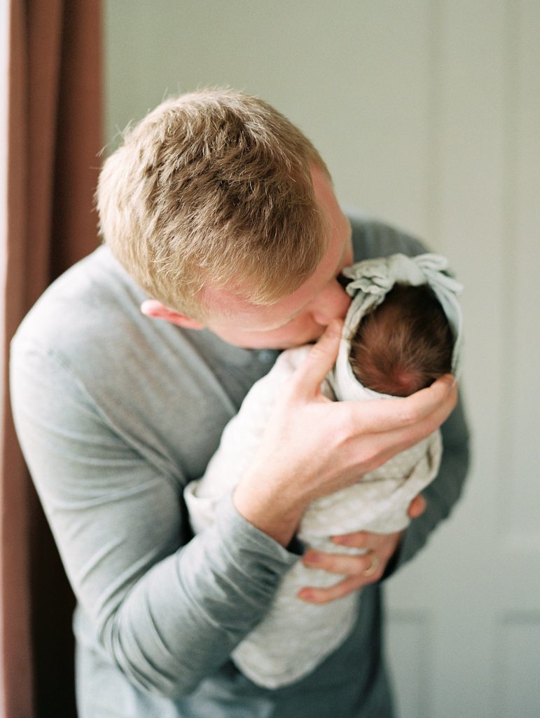 dad kisses swaddled newborn baby on cheek