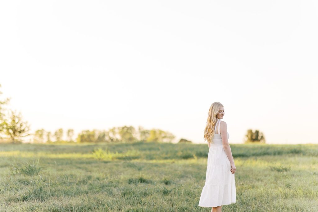 High school senior walks in a field in Oklahoma wearing a long white dress