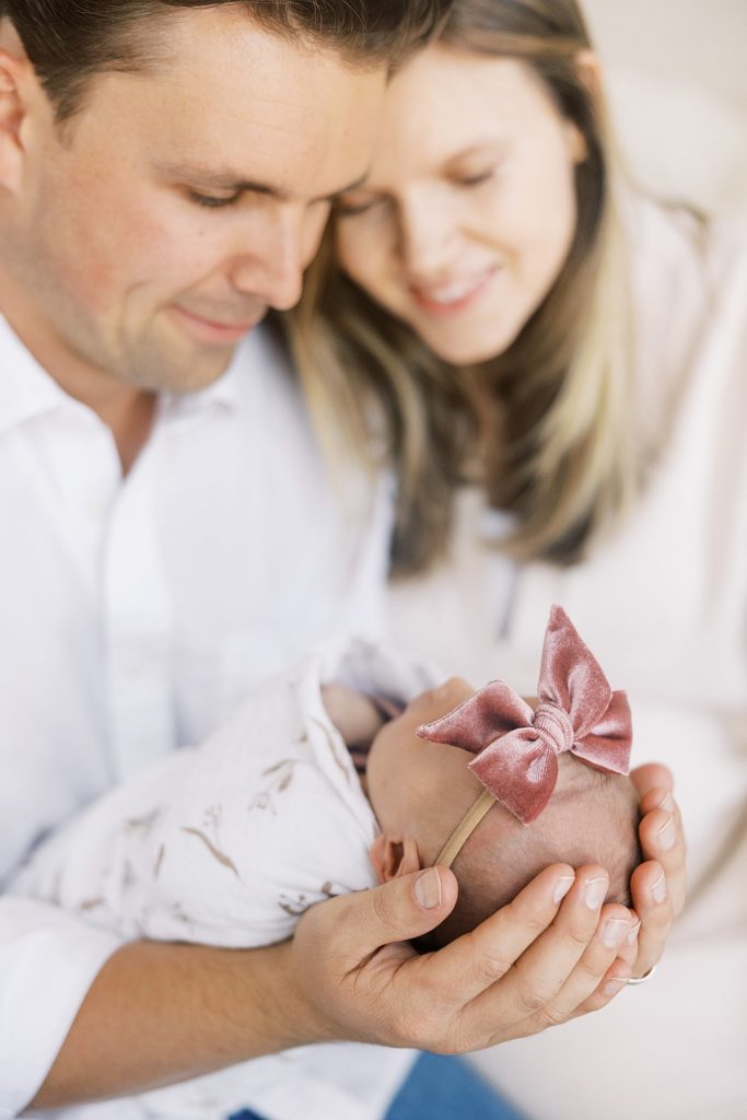 Mom and dad hold newborn baby wearing pink bow during lifestyle newborn photos