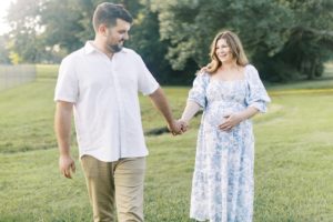 Man leads woman by the hand as they walk during their outdoor maternity photos in the park